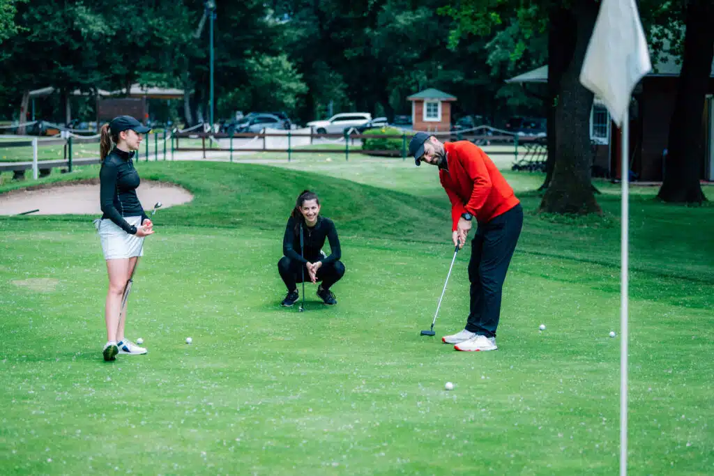 Golf-Putting-Lektion, zwei junge Golferinnen üben mit einem Golflehrer den richtigen Griffdruck beim Putten